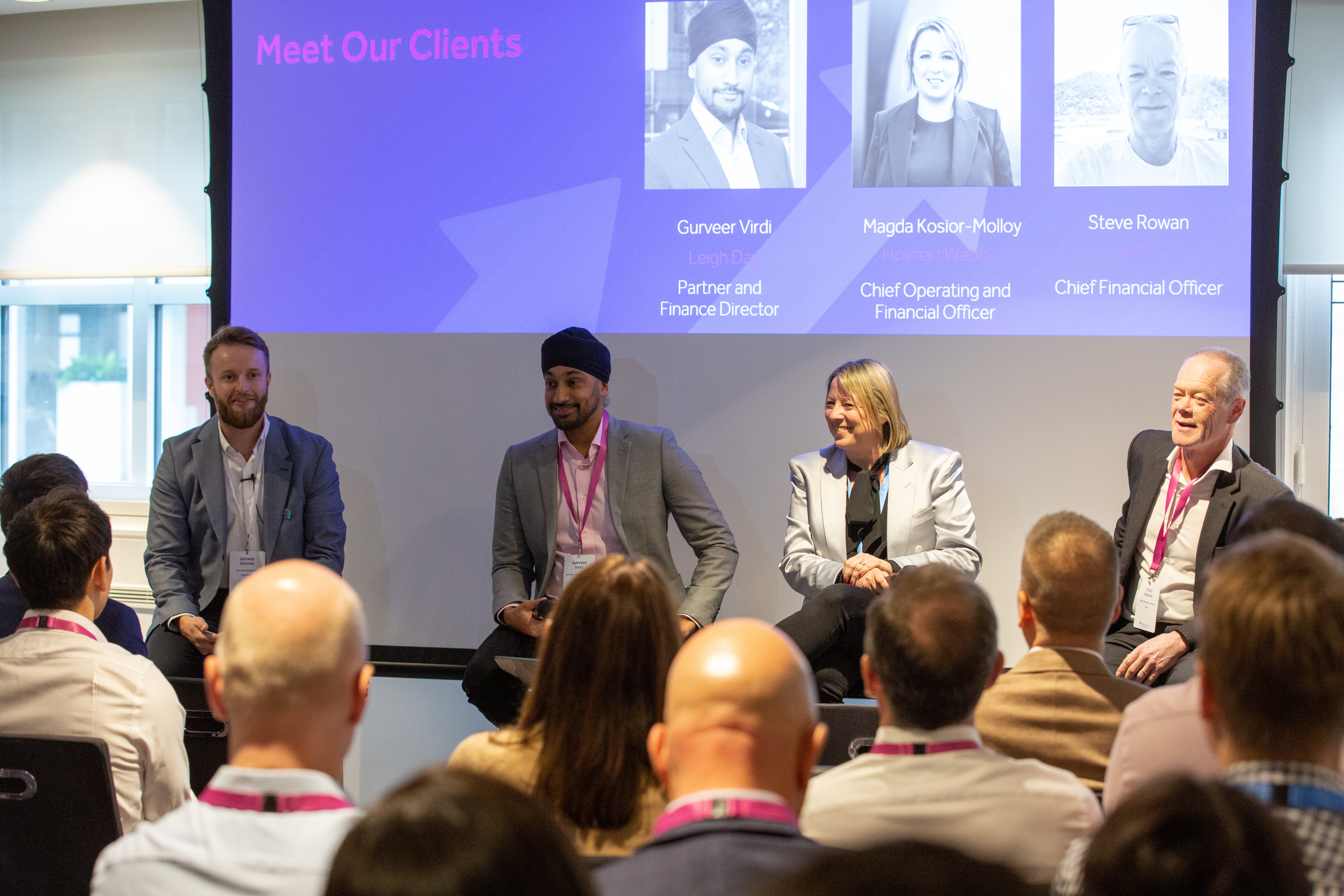 Panellists smile at the front of a crowded room at the BigHand Conference